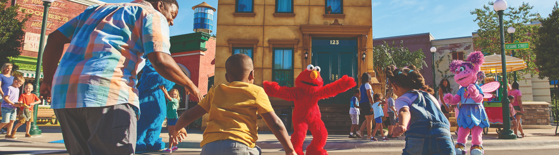 A family runs toward the open arms of Elmo & Abby Cadabby at the Sesame Place San Diego park