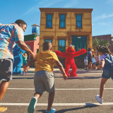 A family runs toward the open arms of Elmo & Abby Cadabby at the Sesame Place San Diego park