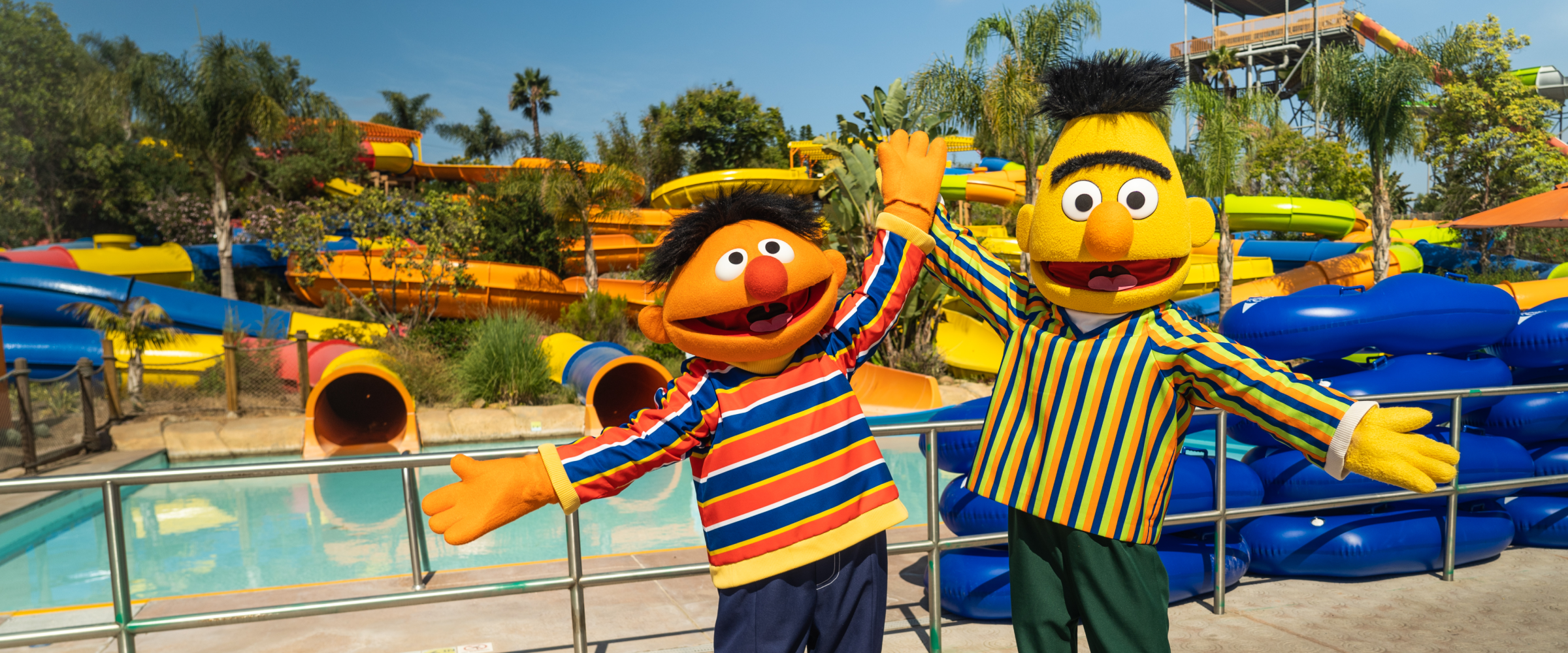 Bert & Ernie stand with open arms in from of Sesame Place water slides