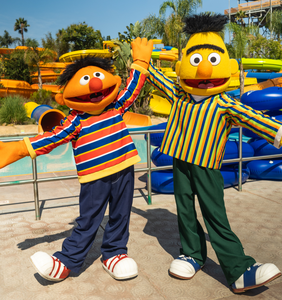 Bert & Ernie stand with open arms in from of Sesame Place water slides
