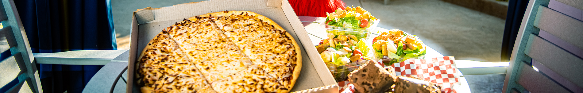 A pizza in a box next to salads